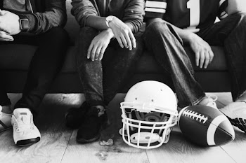 Grayscale Football Helmet on Floor and Man Sit on Sofa