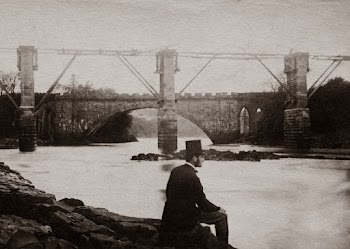 Grayscale Photo Man Wearing A Hat And Suit Sitting By The River Near A Bridge
