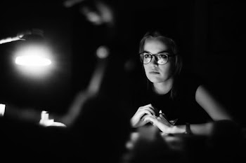 grayscale photo of a woman wearing eyeglasses sitting in front of table