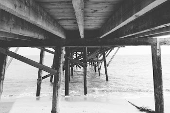 Grayscale Photo of Bridge and Water Near Shore