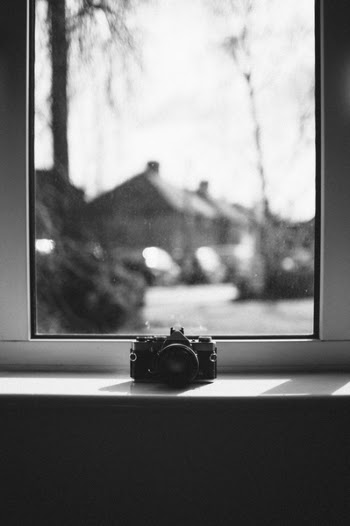 Grayscale Photo of Camera Beside Window