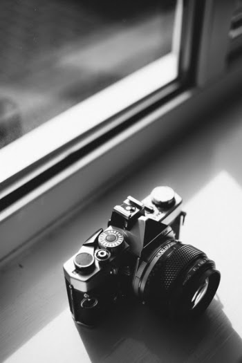 Grayscale Photo of Classical Camera Near Window