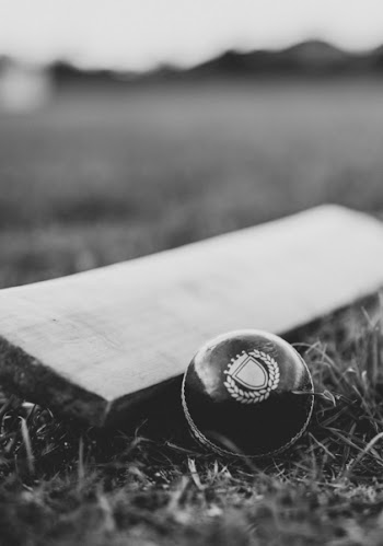 Grayscale Photo of Cricket Ball and Bat on the Ground