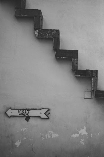 Grayscale Photo of Exit Signage Under Brown Stairs