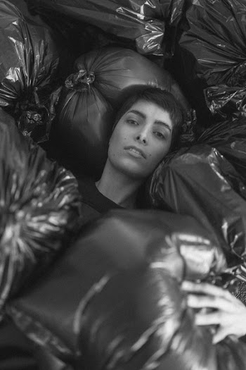 Grayscale Photo of Female Surrounded by Black Plastic Bags