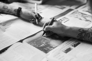 Grayscale Photo of Hands Writing on the Newspaper