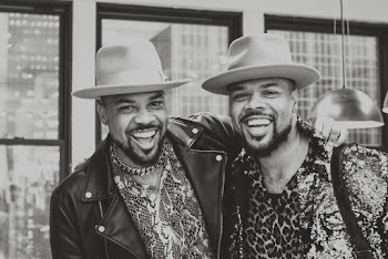 Grayscale Photo of Male Twins in Same Fedora Hats Standing Together