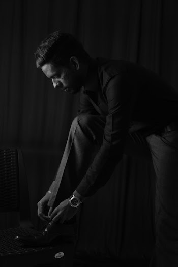 Grayscale Photo of Man in Dress Shirt and Pants Tying His Shoelaces