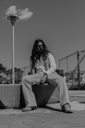 Grayscale Photo of Man in Sunglasses Posing While Sitting on Stone Surface