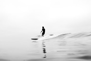 grayscale photo of man riding surfboard on water