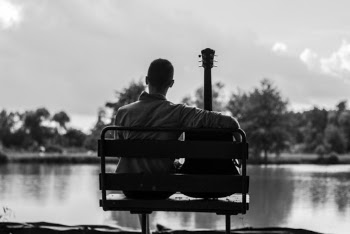 Grayscale Photo of Man Sitting Beside Guitar