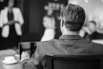 Grayscale Photo of Man Sitting Beside Table