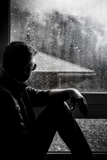 Grayscale Photo of Man Sitting Beside Window 