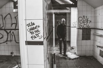 grayscale photo of man standing near white tile wall