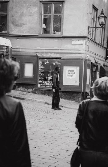 grayscale photo of man standing on road looking at signage