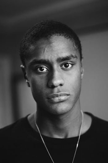 grayscale photo of man wearing black crew-neck top and necklace