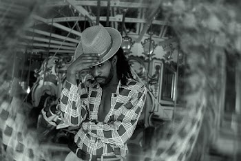 Grayscale Photo of Man Wearing Hat Standing in Front of Carousel