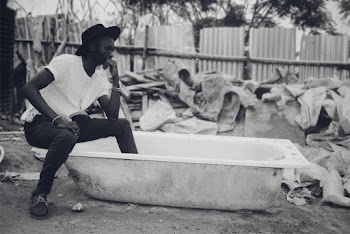 Grayscale Photo of Man Wearing Shirt and Jeans Sitting on Bathtub