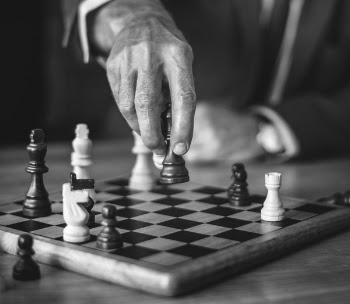 Grayscale Photo of Person Holding Chess Piece