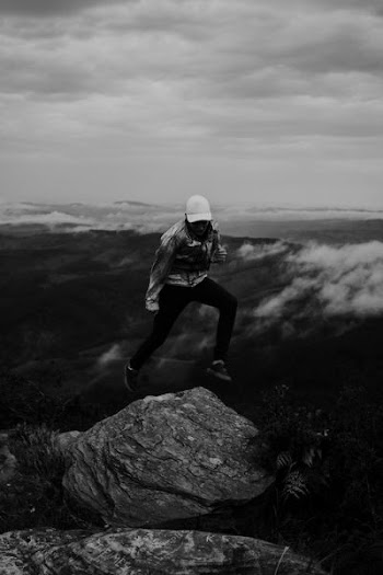 grayscale photo of person jumping on rock