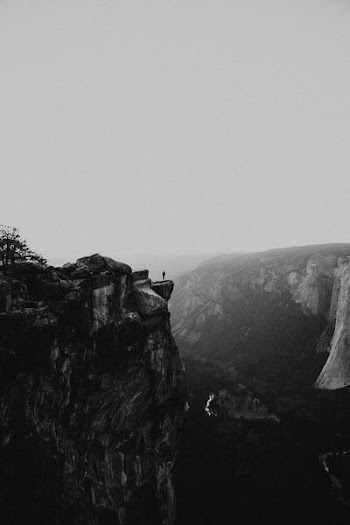grayscale photo of person standing on mountain cliff