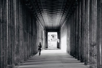 Grayscale Photo of Person Walking Near Columns