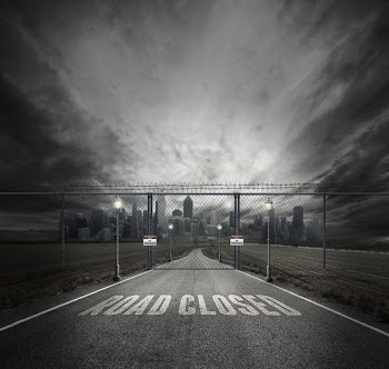 Grayscale Photo of Road Closed on Roadway With Gray Fence Gate in Front of City