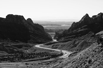 Grayscale Photo of Roadway Surrounded With Rocky Mountains