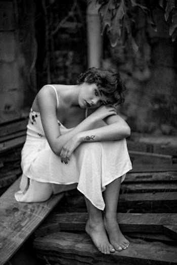Grayscale Photo of Sad Woman Sitting on Wooden Planks While Resting Head on Her Arm