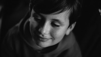 Grayscale Photo of Smiling Boy In a Dark Room Looking Away