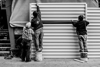Grayscale Photo of Three Men Arranging Metal Wall