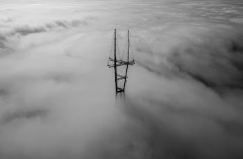 grayscale photo of tower surrounded by clouds