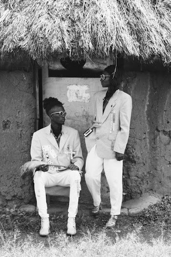 Grayscale Photo of Two Men Standing Near Hut