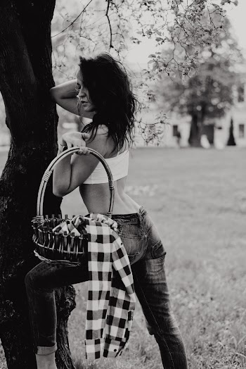 Grayscale Photo of Woman Carrying Basket While Leaning on Tree Posing