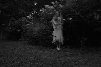 Grayscale Photo of Woman Holding Bouquet of Flowers Beside Plants