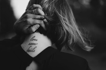 grayscale photo of woman holding her neck while showing Love never Fails tattoo at back
