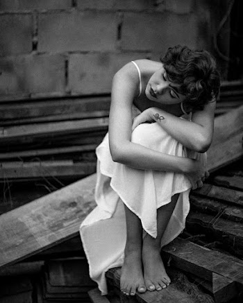 Grayscale Photo of Woman in Dress Sitting on Wooden Plank