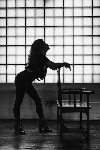 Grayscale Photo of Woman Leaning Forward on Wooden Armchair