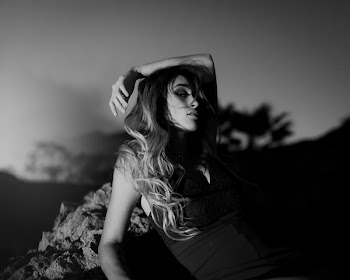 Grayscale Photo of Woman Leaning on Rock
