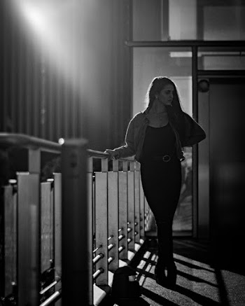 Grayscale Photo of Woman Posing by Metal Railing While Looking Away