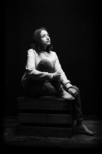 Grayscale Photo of Woman Sitting on a Wooden Crate While Looking Up