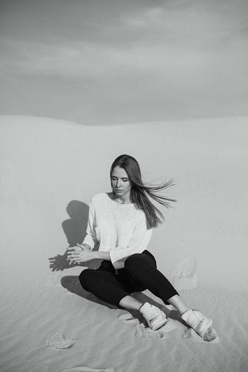 Grayscale Photo of Woman Sitting on Sand Dunes
