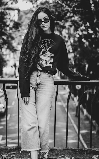 Grayscale Photo of Woman Standing and Leaning on Handrail