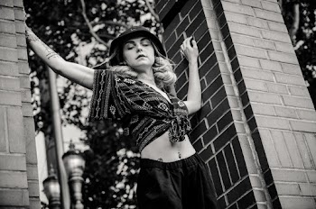 Grayscale Photo Of Woman Standing Between Brick Pillars