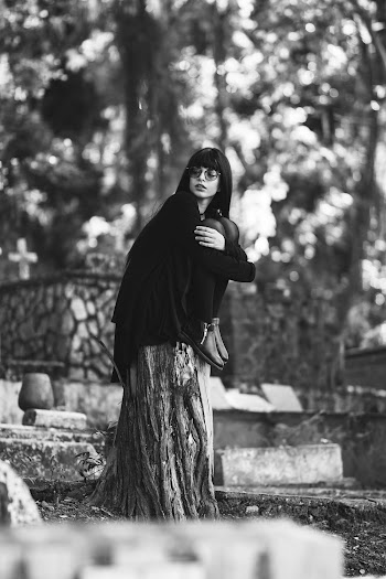 Grayscale Photo of Woman Wearing Black Trench Caot and Black Jeans Sitting on Logs