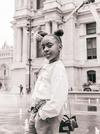Grayscale Photo of Young Girl Posing With Building in the Background