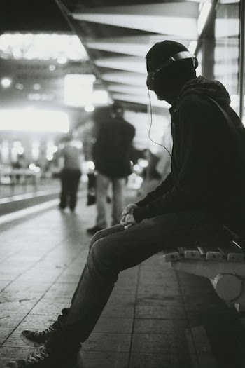grayscale photography of a man sitting on bench while listening music