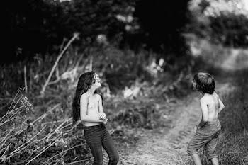 grayscale photography of girl and boy beside bush