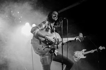 grayscale photography of man about to sing while playing guitar