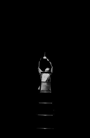 grayscale photography of man climbing ladder fixing the lights